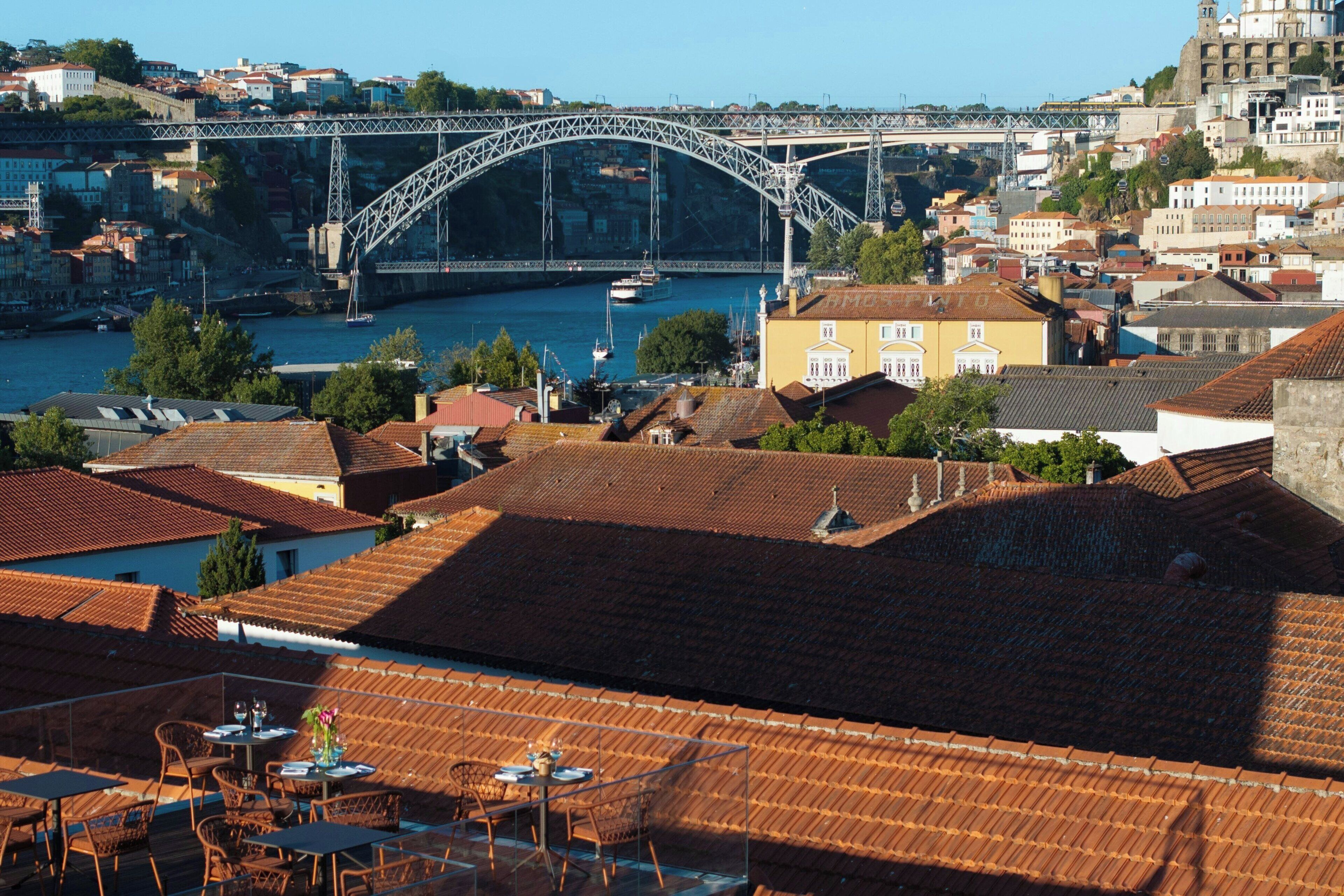 A view of a town with a prominent bridge, terracotta-roofed buildings, and a dining area with tables and chairs.