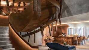 Un interior moderno con una escalera en espiral, una zona de bar y una silla azul.