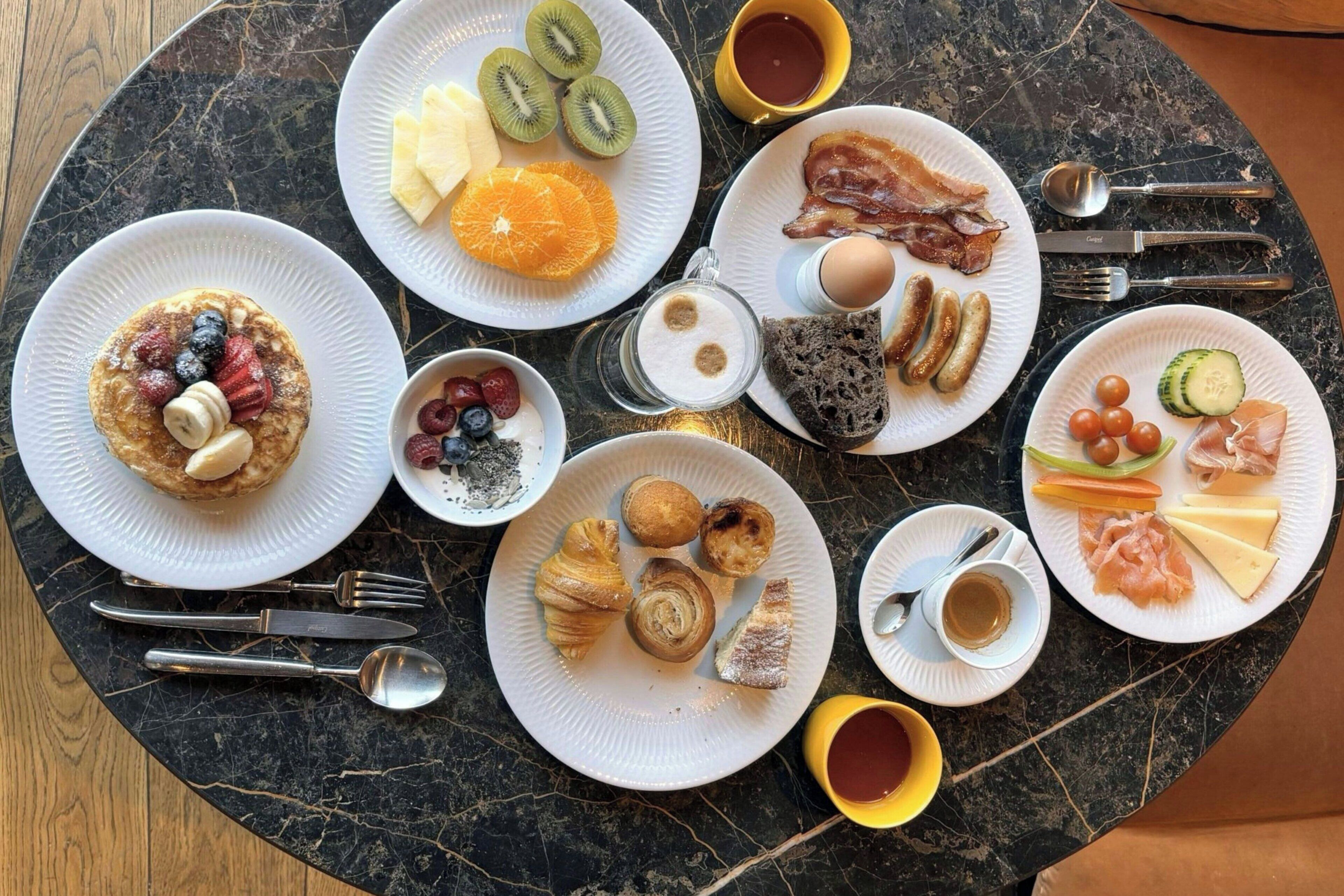 A breakfast spread on a marble table with plates of food, utensils, and condiments.