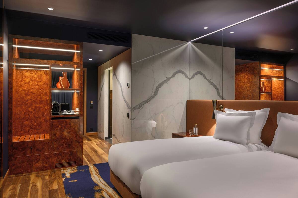 Une chambre d’hôtel moderne dotée d’un grand lit, d’un mur décoratif en bois et d’un mur en marbre agrémenté d’un luminaire.