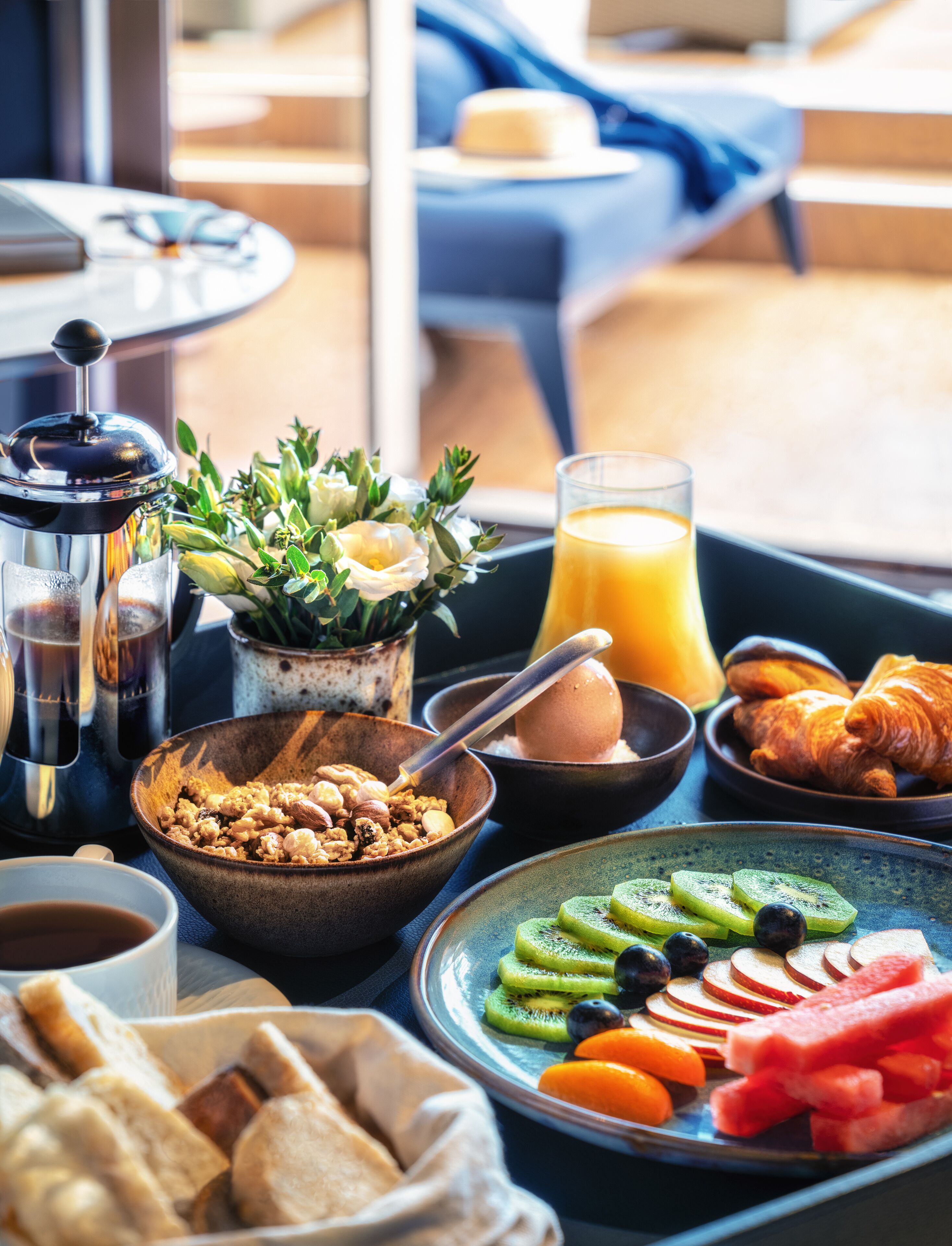 A breakfast table with various food items, a coffee maker, and a glass of orange juice.