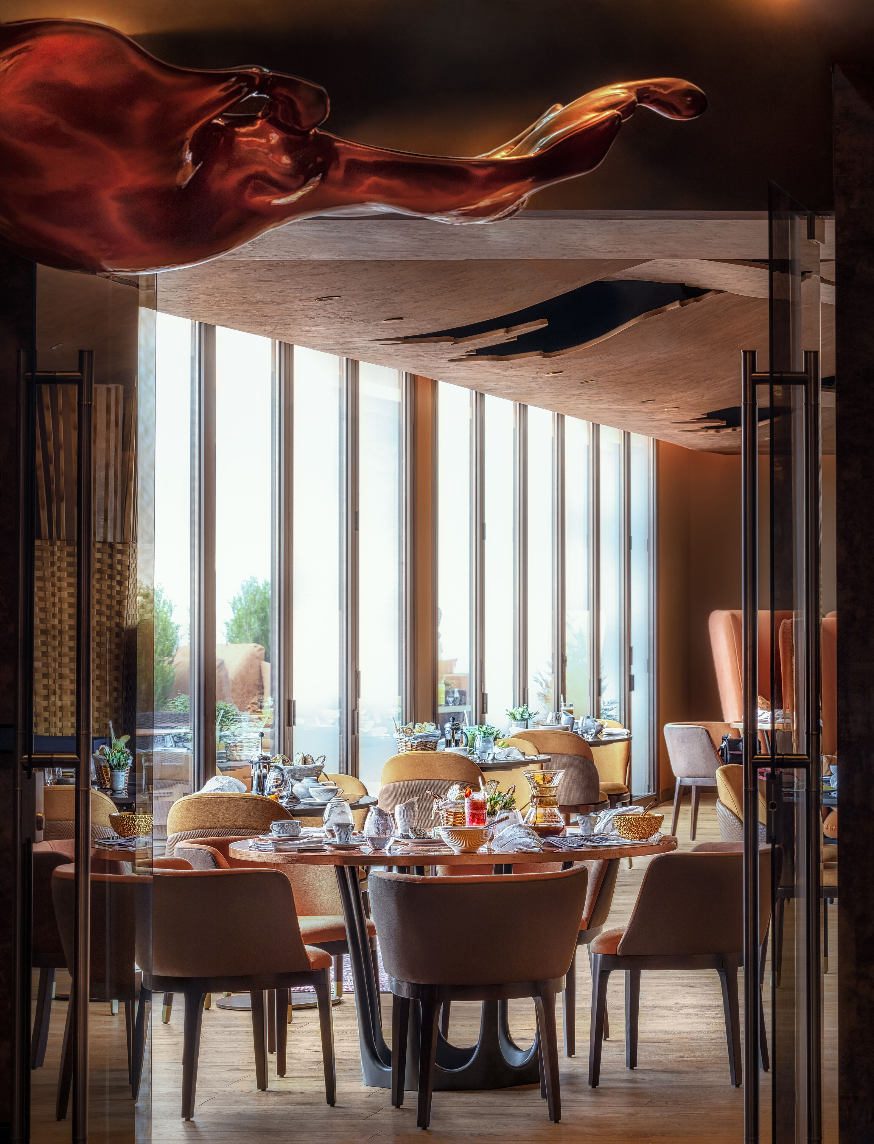 A dining area with a modern interior, large windows, and a unique ceiling sculpture.