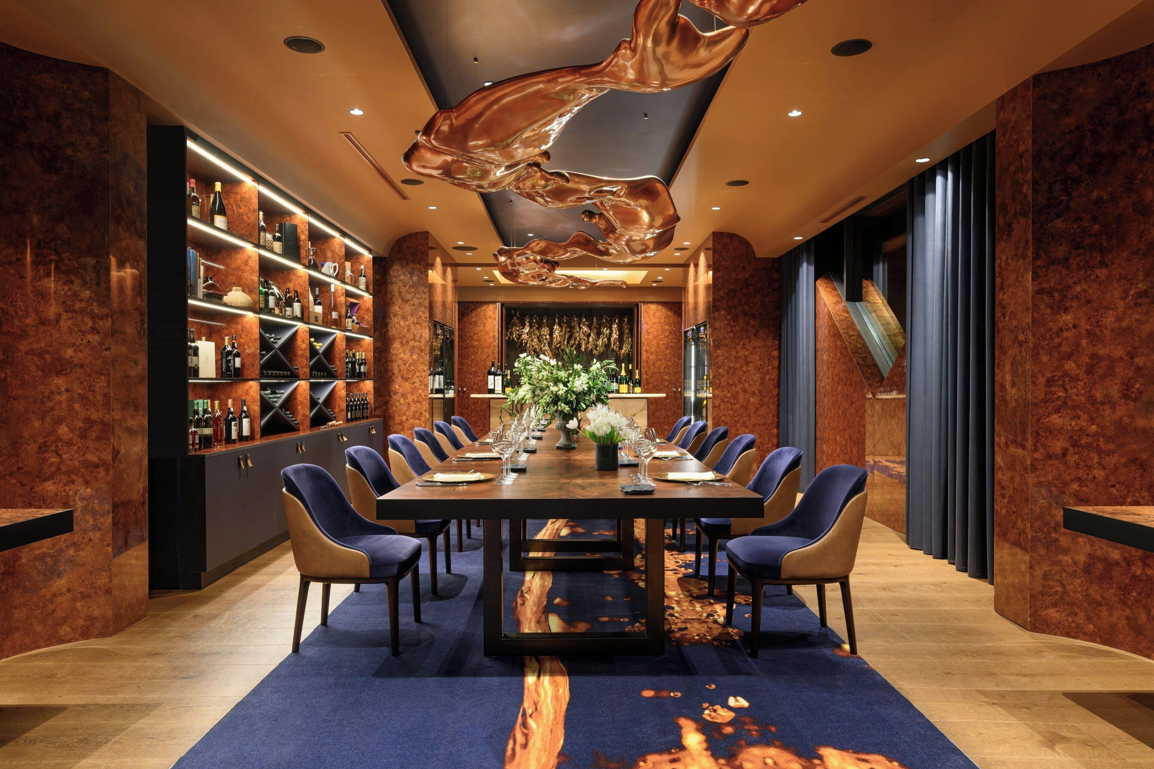 A spacious dining area with a long table, multiple chairs, and a wine rack filled with bottles.