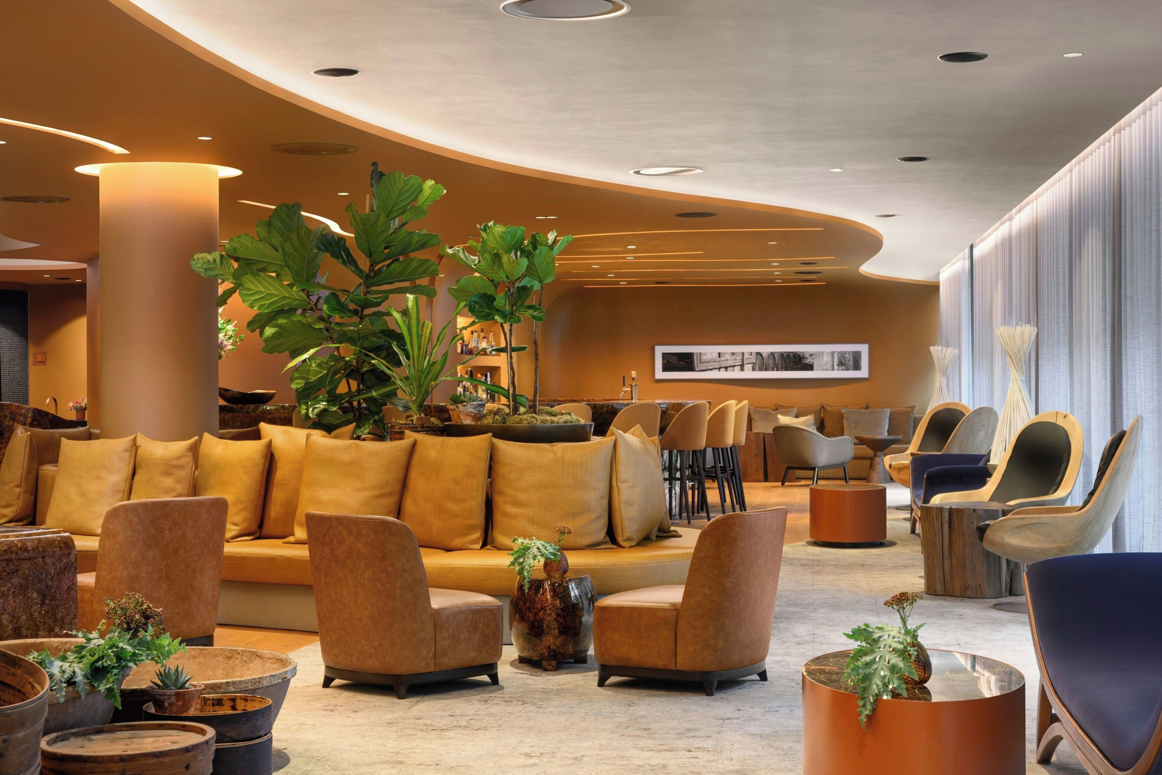 A modern lobby with a curved ceiling, a large sofa, several armchairs, and a coffee table with plants.