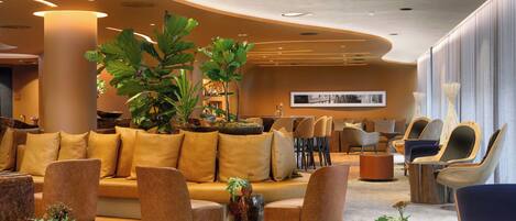 A modern lobby with a curved ceiling, a large sofa, several armchairs, and a coffee table with plants.