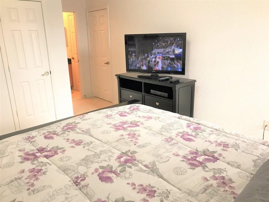 A bedroom with a bed, a TV on a stand, and a door leading to another room.