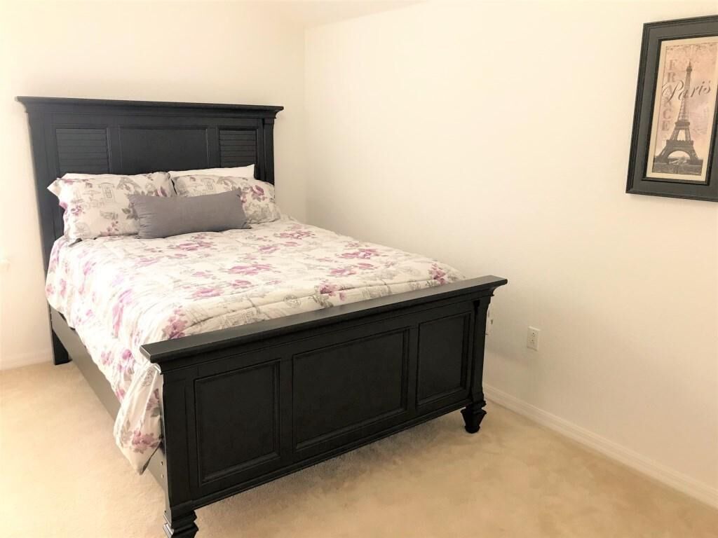 Ein Schlafzimmer mit dunklem Holzbett, floralem Bettbezug und einem gerahmten Bildstuck des Eiffelturms an der Wand.