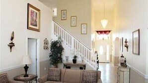 Un salón amplio con un conjunto de sofá color beige, una mesa de centro y una alfombra estampada en rojo y blanco. Una escalera con barandilla blanca conduce a otro nivel.