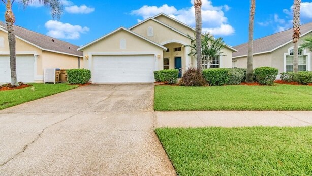 A residential building with a garage, a well-maintained lawn, and palm trees. - Ref 16 Stunning 4 Bed Villa on 5 Star Resort Near Disney (Kissimmee)