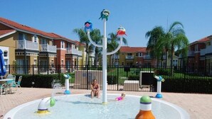 A water play area with multiple water jets and a central pole, surrounded by a paved walkway and residential buildings in the background. - Ref 17 Beautiful 4 Bed Villa With own Poolspa Near Disney (Kissimmee)