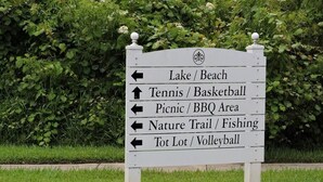 A directional sign with arrows pointing to various recreational areas such as a lake/ beach, tennis/basketball, picnic/BBQ area, nature trail/fishing, and tot lot/volleyball. - Ref 17 Beautiful 4 Bed Villa With own Poolspa Near Disney (Kissimmee)