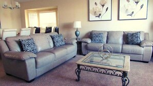 A living room with a grey sofa set, a glass coffee table, and two framed floral paintings on the wall. - Ref 17 Beautiful 4 Bed Villa With own Poolspa Near Disney (Kissimmee)