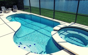 A swimming pool with a hot tub, surrounded by a deck with lounge chairs.