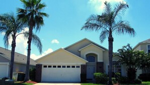 A residential house with a garage, surrounded by palm trees and a well-maintained lawn. - Ref 17 Beautiful 4 Bed Villa With own Poolspa Near Disney (Kissimmee)
