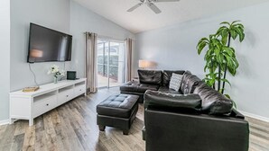 Un salon moderne doté d’un téléviseur à écran plat, d’un canapé en cuir, d’un pouf et d’un ventilateur de plafond.