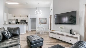 Un salon moderne avec un canapé en cuir, un pouf et un téléviseur à écran plat fixé au mur.