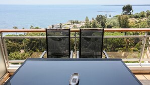 Een balkon met een tafel en stoelen, uitkijkend over de kust.