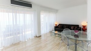 Een moderne woonkamer met een glazen eettafel, transparante stoelen, een zwarte bank en twee lampen.