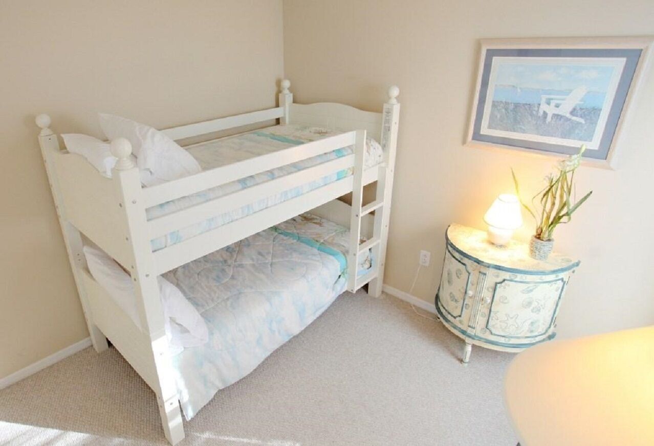 A bunk bed with a lower bunk, a small bedside table with a lamp, and a framed picture on the wall.