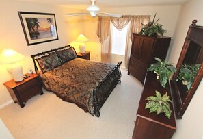 Une chambre à coucher comprenant un lit, des tables de chevet, un ventilateur de plafond, une commode et un miroir.