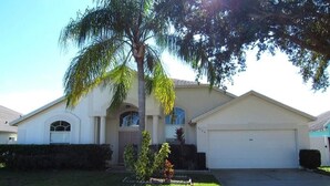 A single-story house with a garage, a front yard with a palm tree, and a small garden area.