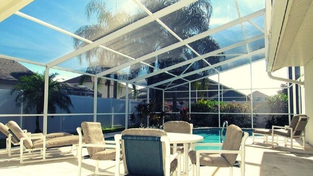 A covered outdoor area with a pool, lounge chairs, and a table.