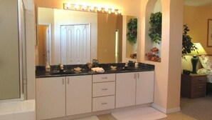 A bathroom with a large mirror, two sinks, white cabinets, and a towel rack.