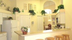 A compact kitchen with a central island, white cabinetry, and a small seating area with stools.