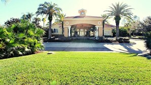 A building with a symmetrical facade, a central clock tower, and a well-maintained lawn with palm trees. - Ref 28 Stunning 4 Bed Villa With own Pool on Gated Resort (Kissimmee)