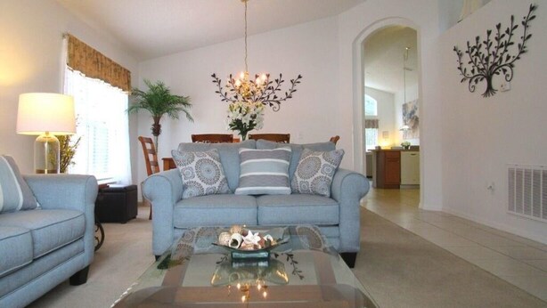 A living room with a sofa, a coffee table, and a chandelier. - Ref 28 Stunning 4 Bed Villa With own Pool on Gated Resort (Kissimmee)