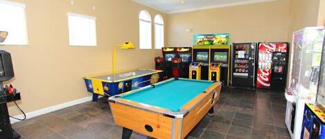 Una mesa de billar en una sala con juegos de arcade y máquinas expendedoras.