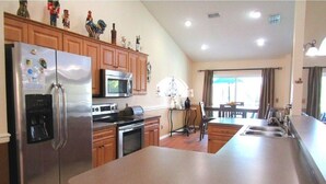 A kitchen with a stainless steel refrigerator, a microwave, and a coffee maker. There is a dining area with a table and chairs. - Ref 43 Family Villa With own Pool Near Disney (Kissimmee)