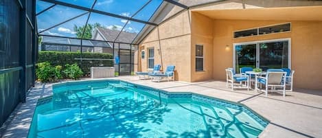 A swimming pool with a glass enclosure, blue lounge chairs, and a patio area with a table and chairs.