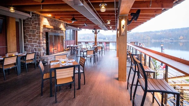 A restaurant with a stone fireplace, wooden tables and chairs, and a view of a lake. - Ghost Light Inn (New Hope)