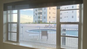 Une vue à travers la fenêtre d’un bâtiment doté d’une piscine, d’un espace de détente extérieur et de plusieurs balcons.