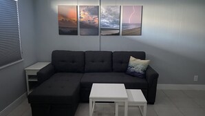 Un salon comprenant un canapé d’angle, une petite table blanche et trois œuvres d’art encadrées accrochées au mur.