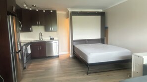 Una habitación funcional con kitchenette, una cama y un mueble pequeño.