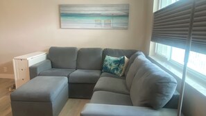 A modern living room with a sectional sofa, a small white cabinet, and a painting of a beach scene. - Sudio Apt Right on the Beach! (Lauderdale by the Sea)