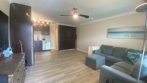 Una sala de estar con un sofá gris, un mueble de madera y un ventilador de techo.