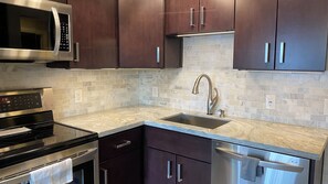 A modern kitchen with stainless steel appliances, dark wooden cabinets, a marble countertop, and a built-in sink. - Sudio Apt Right on the Beach! (Lauderdale by the Sea)