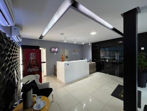 A hotel reception area with a reception desk, a Coca-Cola refrigerator, and a television screen. - MCZ Hotel (Maceió)