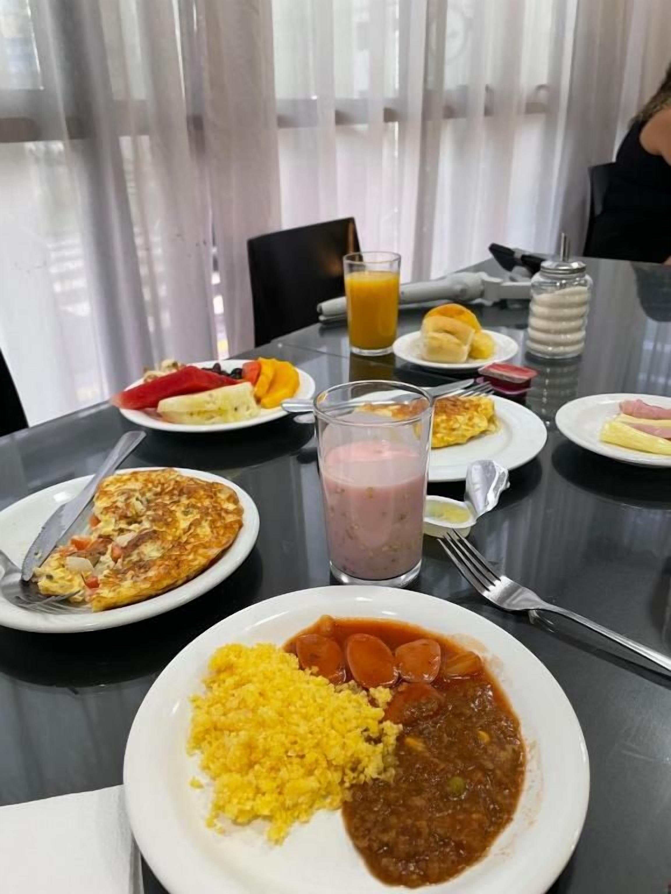 A dining table with plates of food, a glass of juice, and a bottle of water.