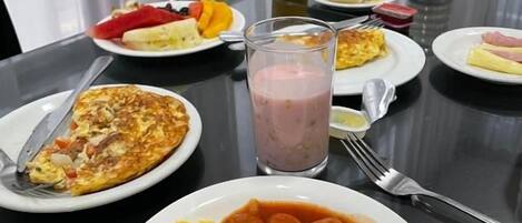A dining table with plates of food, a glass of juice, and a bottle of water.