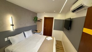 Una habitación de hotel con cama, mesita de noche, lámpara, televisor y aire acondicionado.