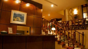 A reception area with a wooden counter, a framed painting, and a staircase with wooden railings and chairs. - Hotel Montecassino (Capilla del Monte)