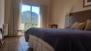A bedroom with a large bed, a view of mountains through the window, a chair, and a radiator. - Hotel Montecassino (Capilla del Monte)