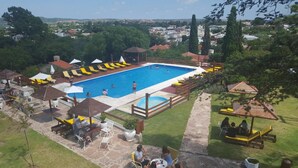 A swimming pool with a wooden deck, lounge chairs, and umbrellas. - Hotel Montecassino (Capilla del Monte)
