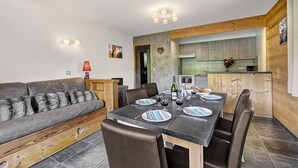 A modern living room with a sofa, dining table, and chairs. There is a kitchen area with cabinets and a stove.