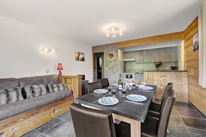 A modern living room with a sofa, dining table, and chairs. There is a kitchen area with cabinets and a stove.