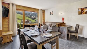 Un coin repas avec une table dressée pour deux personnes, un canapé et un téléviseur fixé à un mur en bois.